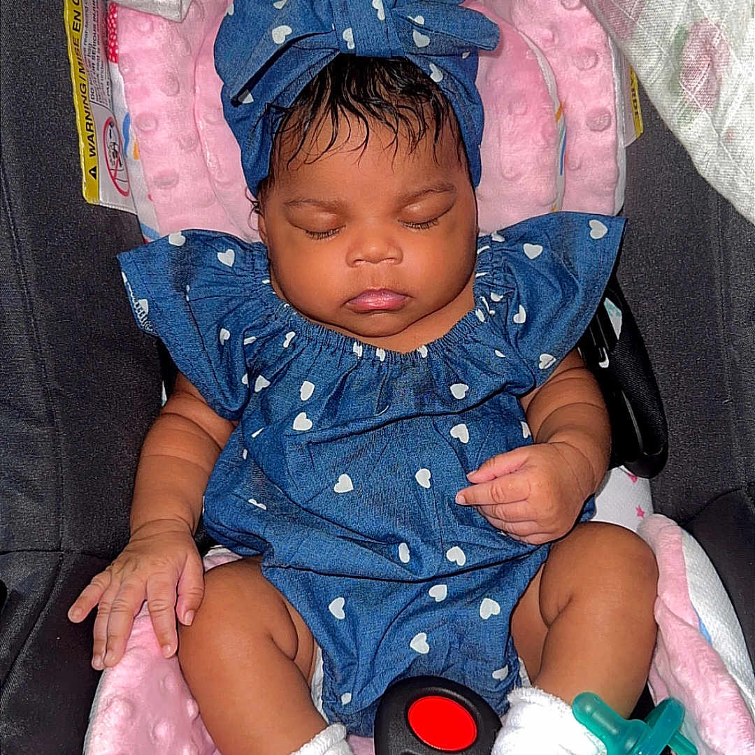 Jorielle is registered to the contest to win money with this photo: baby, infant, sleeping, car_seat, blue_outfit, headwrap, white_socks, pacifier, pink_cushion, child, cute, cozy, adorable, indoor, soft_texture, peaceful, resting, clothing, seat_belt, portrait