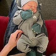 Sylus is registered to the contest to win money with this photo: baby, infant, sleeping, onesie, mittens, booties, dinosaur, hat, hand, lap, jeans, sweater, couch, carpet, indoor, person, cozy, cute, resting, child