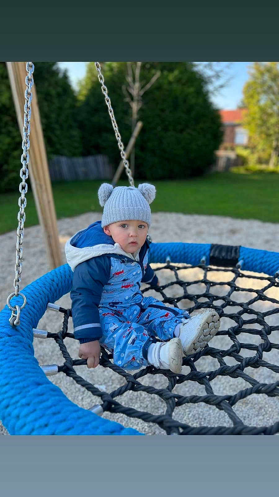 Lyzio a rejoint le concours — aidez-le/la à gagner de superbes lots ! child, toddler, swing, playground, rope_swing, blue, hat, knit_hat, bear_ears, snowsuit, shoes, outdoor, grass, trees, fence, daylight, curious, seated, play, park