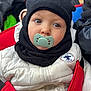 Lyzio participe au concours pour gagner de l'argent avec cette photo : baby, child, pacifier, white_jacket, black_hat, stroller, red_stroller, outdoor, winter_clothing, face, headwear, infant, cute, warm_clothing, person, portrait, closeup, seated, young_child, curious