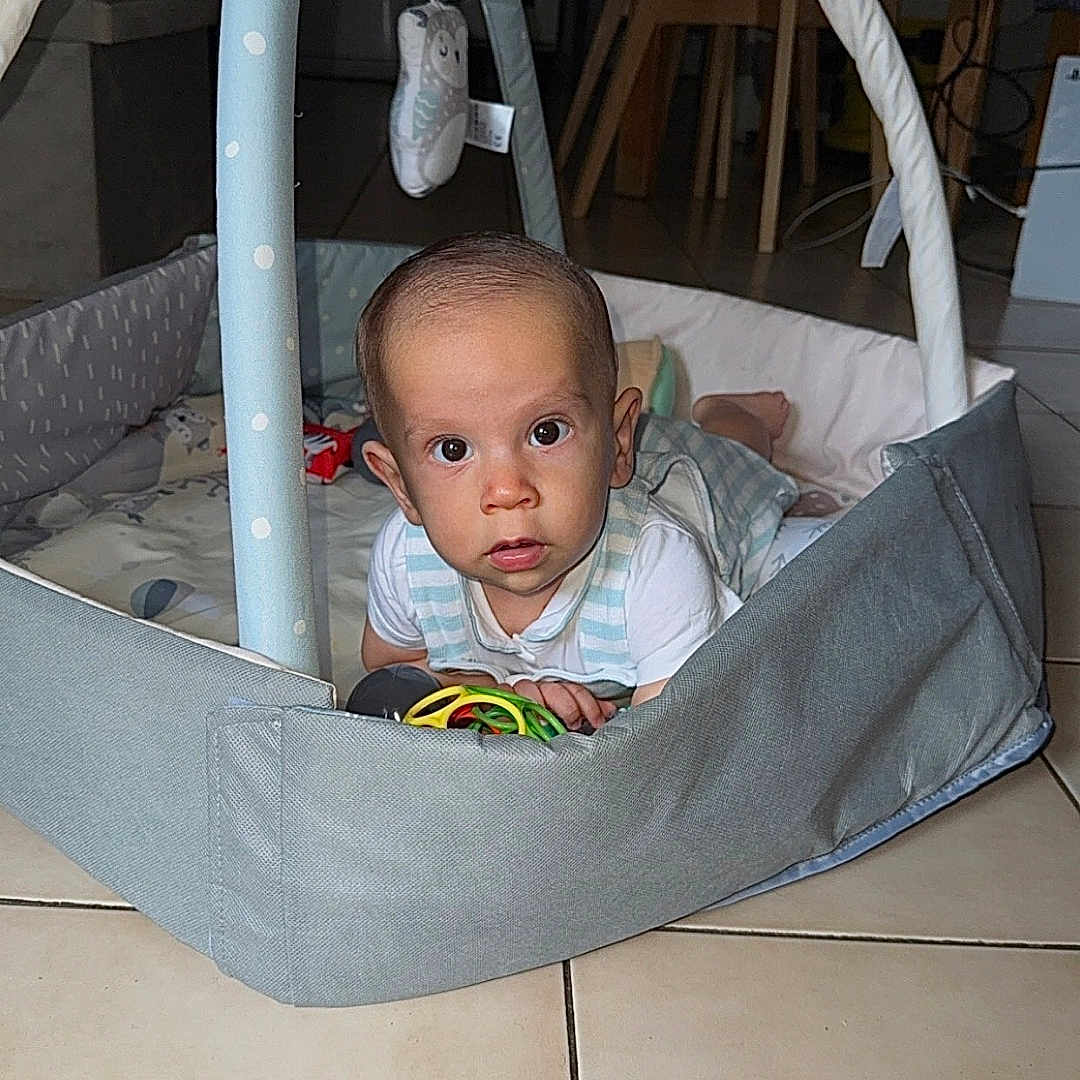 Tiano a rejoint le concours — aidez-le/la à gagner de superbes lots ! baby, baby_toy, child, clothing, crawling, curious, face, floor, furniture, head, home, indoor, infant, looking, person, playpen, soft_play_area, tiled_floor, toy, wide_eyes