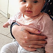 Iris participe au concours pour gagner de l'argent avec cette photo : baby, child, infant, pink_bow, hand, tattoo, nail_polish, clothing, long_sleeve, leggings, indoor, floor_tiles, person, holding, seated, cute, curious, portrait, skin, face