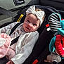 baby, child, car_seat, headband, bow, smile, plush_toy, seatbelt, car_interior, sunlight, white_clothing, infant, toy, happy, cute, safety, vehicle, seat, child_safety, portrait