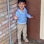 Liam joined the competition — help win amazing prizes! child, boy, smiling, waving, blue_sweater_vest, striped_shirt, beige_pants, shoes, brick_wall, wooden_panel, corner, outdoor, standing, happy, cute, person, casual, daylight, young, portrait