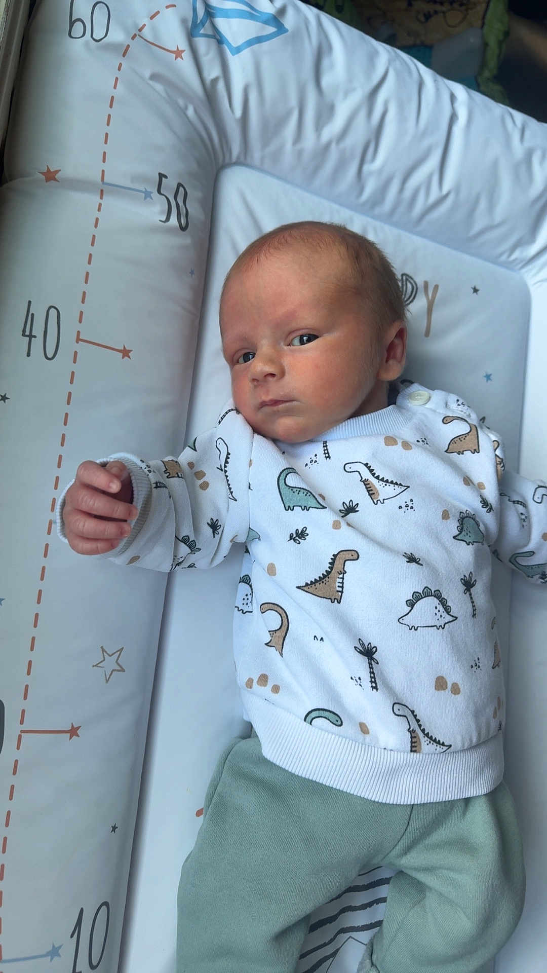 Thaylo a rejoint le concours — aidez-le/la à gagner de superbes lots ! baby, newborn, infant, onesie, dinosaur_print, changing_mat, measurement_marks, lying_down, looking_at_camera, hand, eyes_open, soft_lighting, cozy, blanket, portrait, skin, head, nursery, pajamas, sleepy