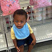 Jaceyon is registered to the contest to win money with this photo: child, toddler, boy, sitting, face, portrait, curious, indoors, store, shopping, retail, shelf, craft_supplies, pink, gift_bags, bib, yellow_shirt, blue_clothing, sandals, floor