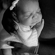 Aniyah is registered to the contest to win money with this photo: baby, newborn, black_and_white, portrait, sleeping, headband, knit_wrap, hand, adult_hand, closeup, infant, peaceful, tender, love, protection, soft_texture, delicate, human, skin, wrapping