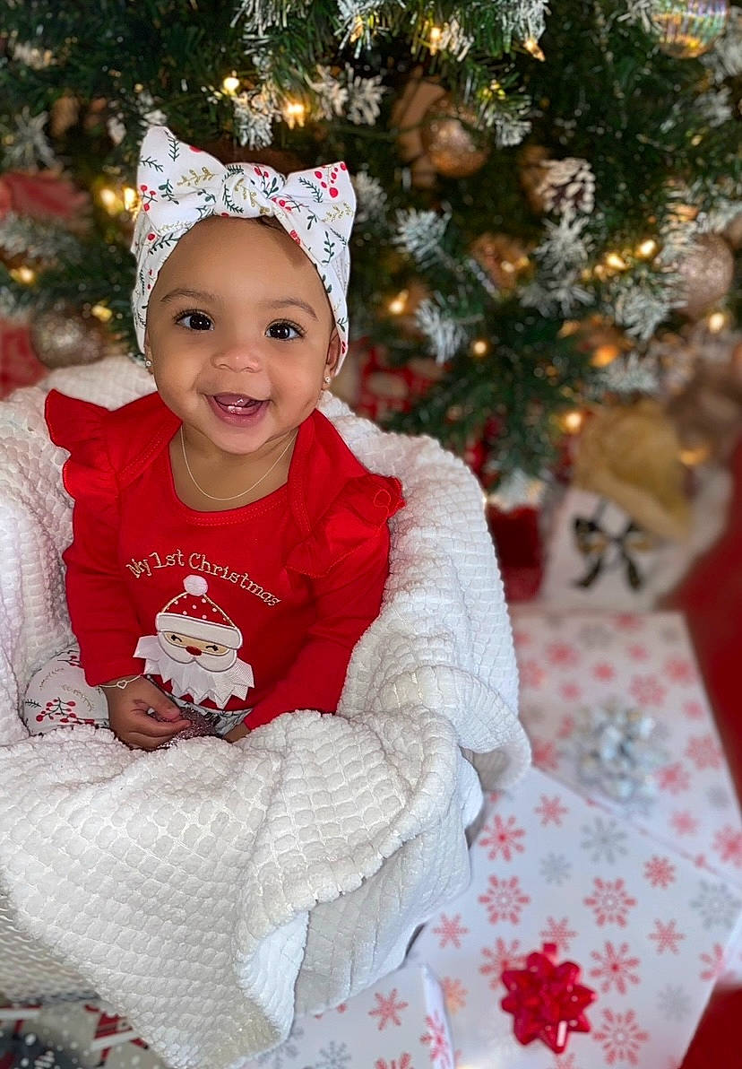 Laylani is registered to the contest to win money with this photo: baby_toddler_clothing, child, christmas, christmas_decoration, christmas_eve, christmas_ornament, christmas_tree, costume_hat, embellishment, event, face, happy, head, headwear, holiday, holiday_ornament, joy, ornament, person, pink