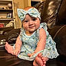 baby, child, infant, dress, headband, floral_pattern, blue, smile, leather_couch, living_room, furniture, person, foot, hand, indoors, sitting, cute, portrait, happy, home