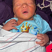 Anakin is registered to the contest to win money with this photo: newborn, baby, sleeping, blanket, blue_onesie, crown_graphic, hands, face, closed_eyes, cozy, purple_background, striped_blanket, infant, peaceful, portrait, soft_lighting, indoors, cute, child, wrapped