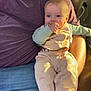 baby, child, man, beard, sitting, couch, indoor, clothing, vest, pants, smiling, thumb_in_mouth, blue_eyes, furniture, relaxed, casual, human, person, home, comfort
