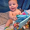 baby, child, diaper, toy, soft_book, blue_background, tent, sitting, smiling, happy, indoor, plush_toy, colorful, curious, infant, person, cute, playtime, fabric, reading