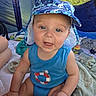 baby, child, blue_clothing, hat, camouflage, tent, blanket, toy, indoor, smiling, sitting, face, person, infant, cute, summer, headwear, expression, playtime, light