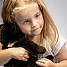 child, girl, toddler, portrait, smiling, face, blue_eyes, blonde_hair, braided_hair, long_hair, teddy_bear, stuffed_animal, hugging, indoors, soft_lighting, closeup, white_shirt, hands, sitting, photography