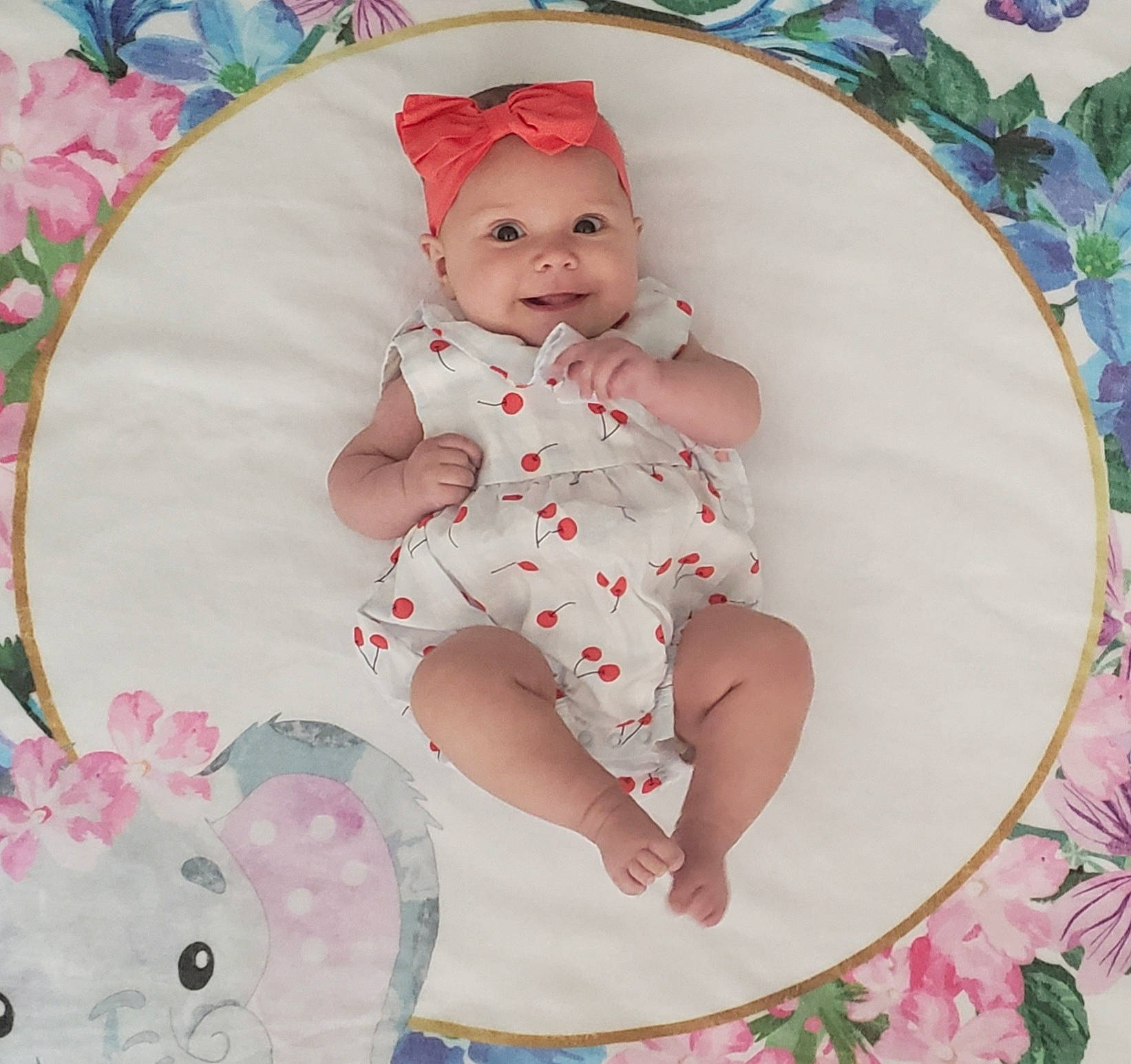 Harleen is registered to the contest to win money with this photo: arm, baby, baby_products, baby_toddler_clothing, cheek, child, dress, happy, headgear, headwear, human_body, joy, lap, linens, pattern, person, petal, pink, skin, sleeve