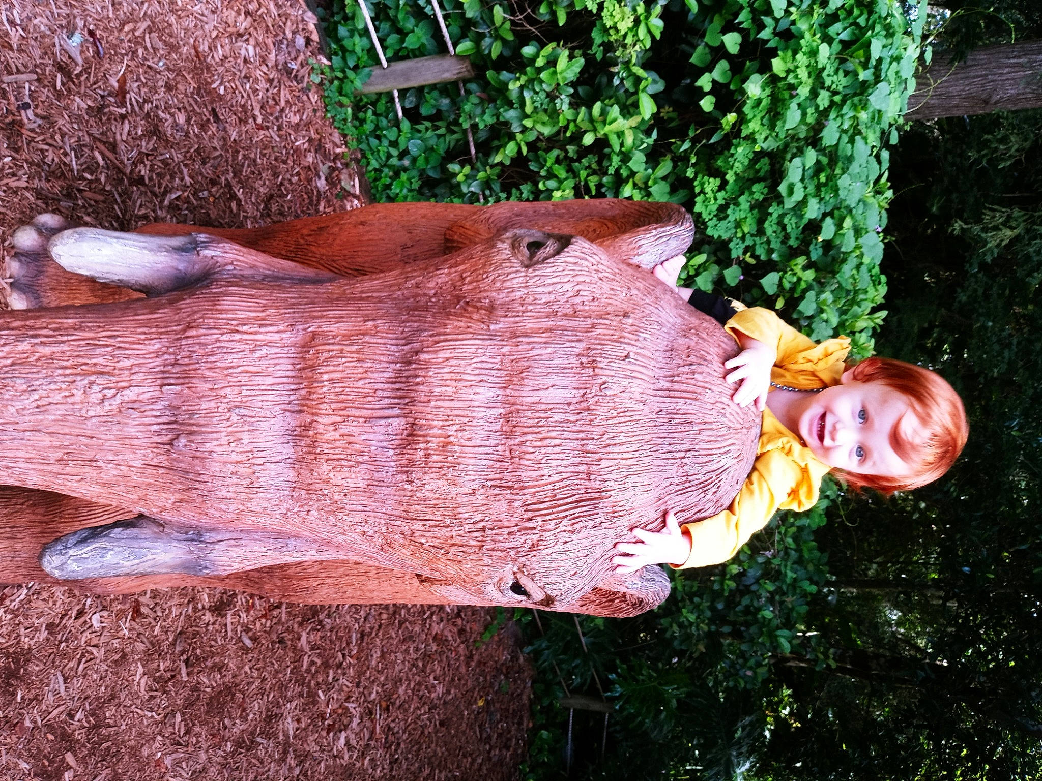 Cynthia is registered to the contest to win money with this photo: art, brick, carving, flesh, garden, grass, joy, lawn_ornament, leisure, people_in_nature, person, plant, sculpture, shrub, smile, statue, trunk, wood, wool, yard