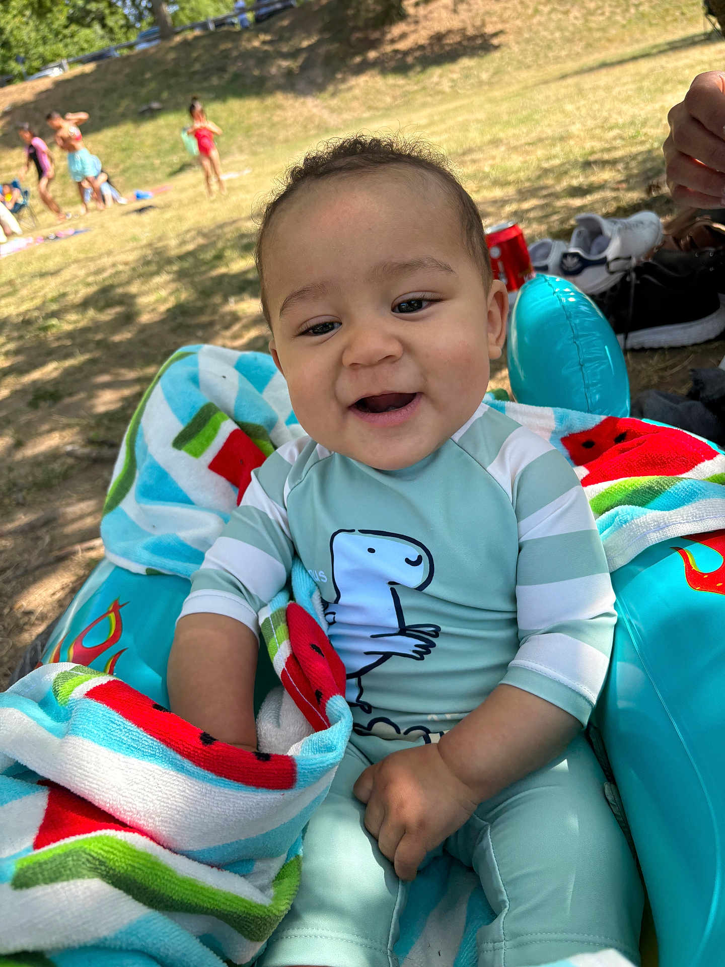 Dahion Rios a rejoint le concours — aidez-le/la à gagner de superbes lots ! toddler, child, baby, smiling, outdoor, park, grass, sunlight, inflatable_chair, towel, watermelon_pattern, swimsuit, dinosaur, happy, people, summer, shoes, relaxing, play, family