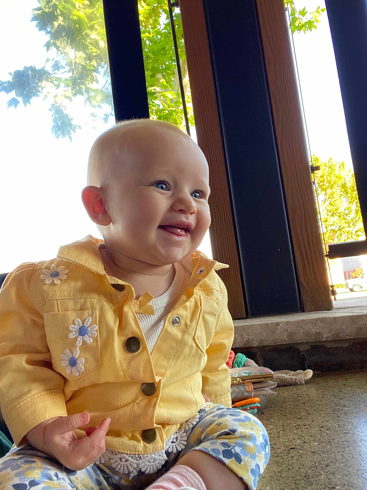 Juliette is registered to the contest to win money with this photo: baby, child, smiling, yellow_jacket, embroidered_flowers, indoor, window, natural_light, blue_eyes, happy, cute, sitting, clothing, person, infant, floor, patterned_pants, hand, face, portrait