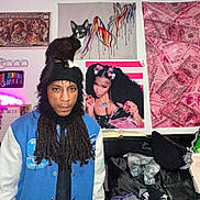 Nino is registered to the contest to win money with this photo: blue_jacket, cat, clutter, cute_cat, decor, dreadlocks, hat, indoor, jacket, money_print, neon_light, person, pet, pet_on_head, pink_tapestry, portrait, poster, room, shelf, wall_art