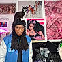 blue_jacket, cat, clutter, cute_cat, decor, dreadlocks, hat, indoor, jacket, money_print, neon_light, person, pet, pet_on_head, pink_tapestry, portrait, poster, room, shelf, wall_art