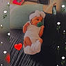 baby, infant, pacifier, white_clothing, headband, pillow, bed, couch, indoor, decorative_overlay, flower_pattern, red_heart_emoji, cute, child, resting, small_person, face, hands, feet, soft_lighting