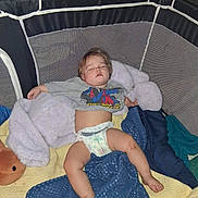 Jordan is registered to the contest to win money with this photo: toddler, sleeping, playpen, blanket, plush_toy, diaper, shirt, spiderman, child, resting, indoors, cozy, nap, cute, baby, soft_toy, comfort, relaxation, young_child, casual