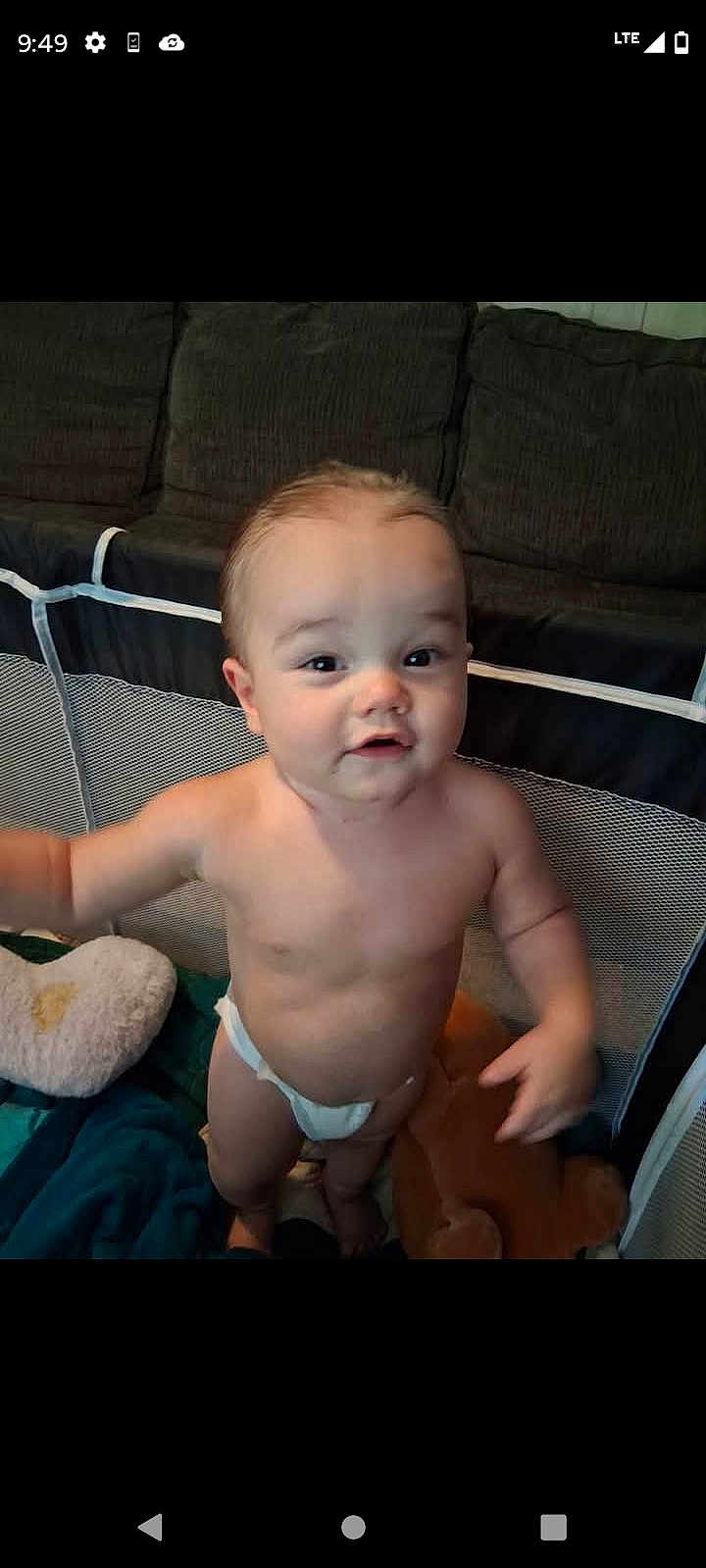 Jordan is registered to the contest to win money with this photo: baby, diaper, playpen, plush_toy, pillow, infant, child, indoor, couch, face, person, standing, curious, young_child, home, soft_toy, mesh, background, expression, bare_chest