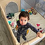 Thomas is registered to the contest to win money with this photo: toddler, child, playpen, plush_toys, indoor, floor, wooden_floor, curly_hair, pajamas, standing, looking_up, hand, grip, toys, stuffed_animals, cozy, home, baby, infant, cute