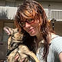Frankie is registered to the contest to win money with this photo: woman, dog, outdoor, sunlight, glasses, building, balcony, affection, pet, holding, smile, face, casual_clothing, leash, paw, red_hair, shadow, daylight, brick_floor, lamp_post