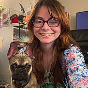 Frankie is registered to the contest to win money with this photo: woman, dog, glasses, smile, indoor, casual, floral_clothing, pet, small_dog, brown_hair, jeans, hand_holding, furniture, television, shoes, floor, earrings, collar, face, happy