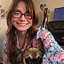 Frankie joined the competition — help win amazing prizes! person, dog, glasses, smiling, indoor, young_adult, brown_hair, small_dog, ear_collar, casual_clothing, patterned_shirt, living_room, chair, television, decorations, happy, pet, holding, portrait, seated