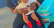 Essence joined the competition — help win amazing prizes! baby, child, parent, father, sitting, lap, stroller, outdoor, crowd, theme_park, mickey_mouse, red_socks, bow, black_clothing, red_shoes, family, portrait, daylight, public_place, happy