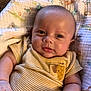 baby, infant, child, face, skin, arm, blanket, striped_clothing, giraffe_patch, lying_down, cute, expression, patterned_blanket, indoors, person, newborn, young_child, small_hand, soft_light, portrait