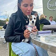 Luna joined the competition — help win amazing prizes! woman, dog, leather_jacket, jeans, outdoor, chair, table, glass_table, hand, pet, leash, people, building, cloudy_sky, green_chair, casual_clothing, portrait, small_dog, accessory, sunglasses