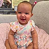 Oaklynn is registered to the contest to win money with this photo: baby, child, smiling, indoor, dress, floral_pattern, pink_blanket, sitting, happy, cute, infant, person, portrait, soft_texture, window_blinds, cozy, natural_light, furniture, skin, head