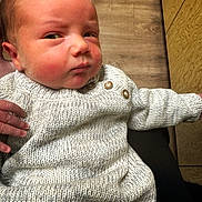 Mason joined the competition — help win amazing prizes! baby, infant, knitted_sweater, hand, wooden_floor, wooden_cabinet, face, expression, person, portrait, indoors, cozy, clothing, cute, newborn, skin, cheeks, looking, sitting, holding