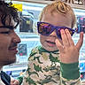 Daelen joined the competition — help win amazing prizes! toddler, child, young_adult, glasses, sunglasses, dinosaur_pajamas, hand, smile, face, curly_hair, store, shelf, light, reflection, person, clothing, indoor, playful, portrait, interaction