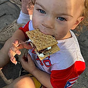 Daelen joined the competition — help win amazing prizes! child, toddler, smore, marshmallow, cracker, food, outdoor, curly_hair, blue_eyes, summer, snack, messy, happy, casual_clothing, red_shirt, shorts, sunlight, hand, face, portrait