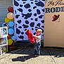 Daelen is registered to the contest to win money with this photo: toddler, child, barefoot, overalls, red_plush, cow_print, balloons, outdoor, concrete, sunlight, celebration, party, signage, smiling, happy, young_child, decorations, playful, daytime, costume
