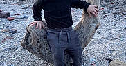Daelen is registered to the contest to win money with this photo: toddler, child, curly_hair, beach, driftwood, rocks, sea, water, sand, outdoor, nature, casual_clothing, black_sweater, gray_pants, blue_shoes, small_child, portrait, daytime, playful, scenic
