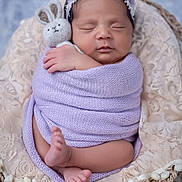 Sandra Isabelle is registered to the contest to win money with this photo: newborn, baby, sleeping, swaddled, plush_toy, bunny, basket, lace, pom_poms, purple_wrap, headband, flower_headband, infant, peaceful, cute, soft_texture, portrait, close_up, indoor, cozy