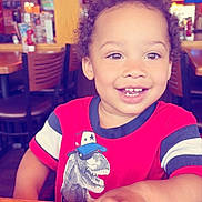 Ezariah is registered to the contest to win money with this photo: toddler, child, smiling, curly_hair, red_shirt, dinosaur_graphic, restaurant, table, wooden_chair, menu, indoor, happy, portrait, person, casual_clothing, dining, cute, young_child, bright_lighting, family