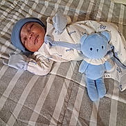 Da'Rell is registered to the contest to win money with this photo: newborn, baby, sleeping, infant, portrait, bed, blanket, checkered, plush_toy, stuffed_animal, blue_toy, onesie, mittens, hat, clothing, cozy, indoors, nursery, lying_down, peaceful
