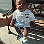 Kycen is registered to the contest to win money with this photo: baby, child, bench, wood, carving, mickey_mouse, clothing, sandals, outdoor, sunlight, shadow, person, cute, curious, smile, arm, hand, footwear, face, happy