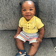 Kycen is registered to the contest to win money with this photo: baby, child, smile, polo_shirt, yellow_shirt, striped_shorts, sandals, navy_shoes, sitting, couch, gray_couch, happy, cute, indoor, portrait, person, young_child, infant, face, legs