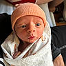 newborn, baby, infant, hat, knit_cap, blanket, wrapped, tattoo, arm, person, skin, face, eyes, indoors, closeup, cute, expression, holding, swaddle, human