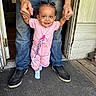 toddler, child, adult, hands, doorway, pink_outfit, socks, smile, first_steps, floor, wooden_floor, jeans, shoes, indoors, door, pacifier_clip, person, helping, happy, standing