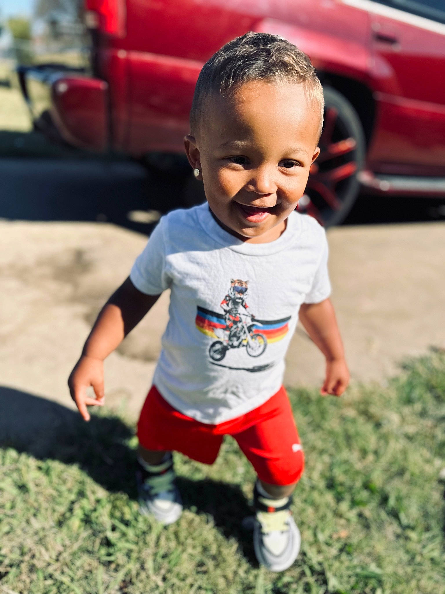 Deonte is registered to the contest to win money with this photo: asphalt, baby_toddler_clothing, car, cool, footwear, fun, grass, hairstyle, happy, joy, leisure, person, red, shoe, shorts, sleeve, smile, standing, tire, toddler