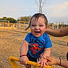 toddler, child, playground, yellow_equipment, outdoor, daylight, smiling, happy, blue_shirt, spiderman, person, hand, support, grass, tree, sky, casual_clothing, playing, fun, park