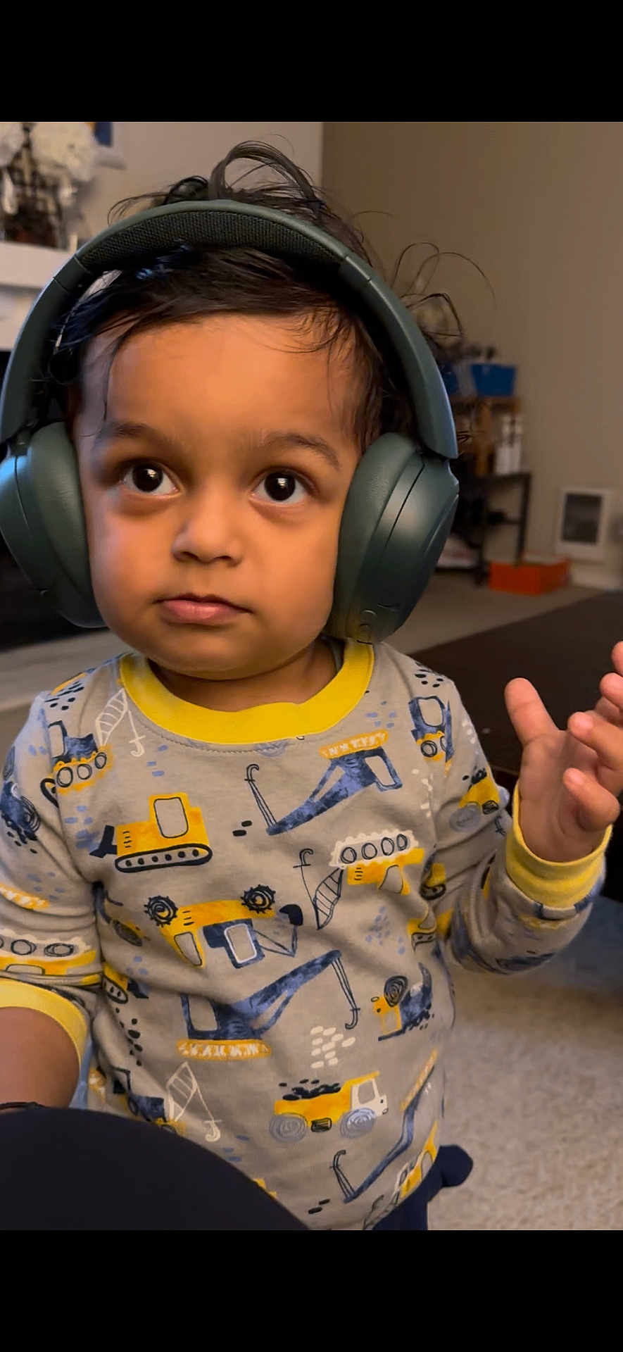 Addie joined the competition — help win amazing prizes! child, toddler, headphones, pajamas, construction_vehicles, indoor, carpet, curly_hair, big_eyes, long_sleeves, yellow, gray, playful, cute, expression, person, young_child, living_room, furniture, hand